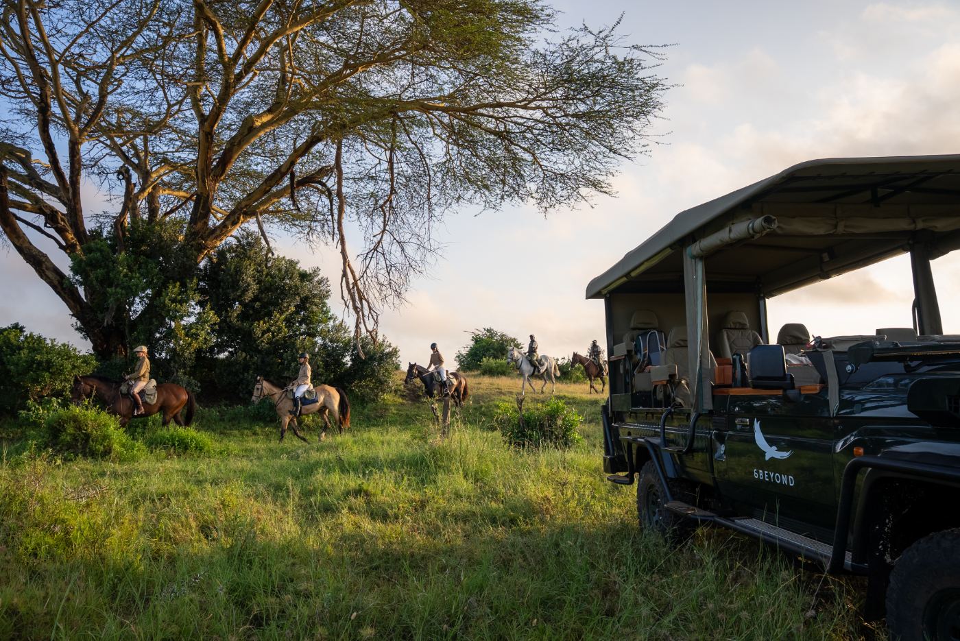 Riders on horseback at dawn beside the safari vehicle